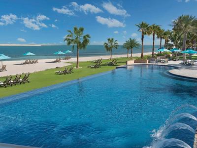 Großer Pool mit Blick auf den Strand und Palmen an einem sonnigen Tag.