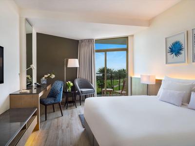 Habitación de hotel moderna con cama grande, área de estar y vista a un paisaje verde.