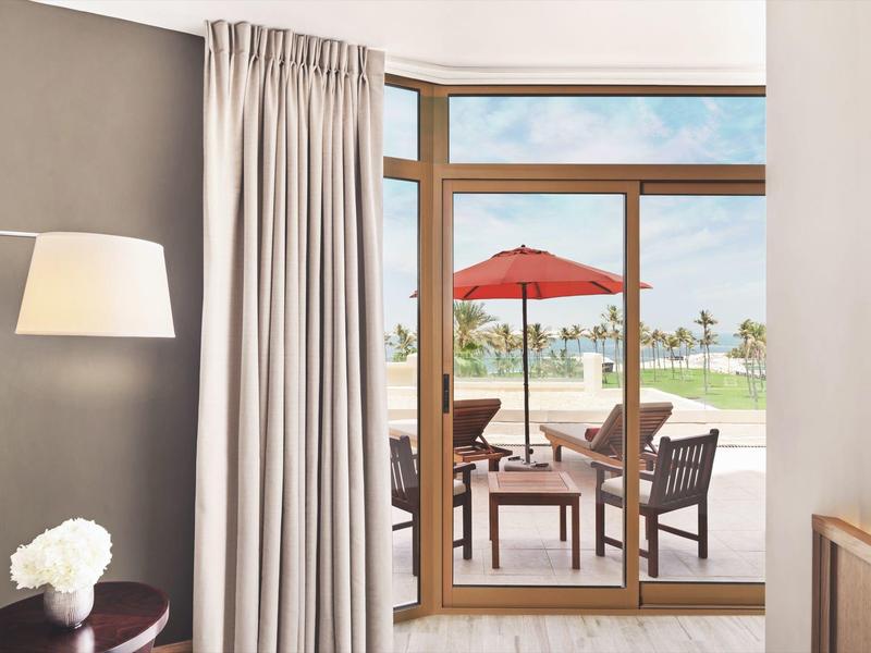 Habitación de hotel luminosa con puerta corredera de cristal y vista a terraza con sombrilla y jardín.