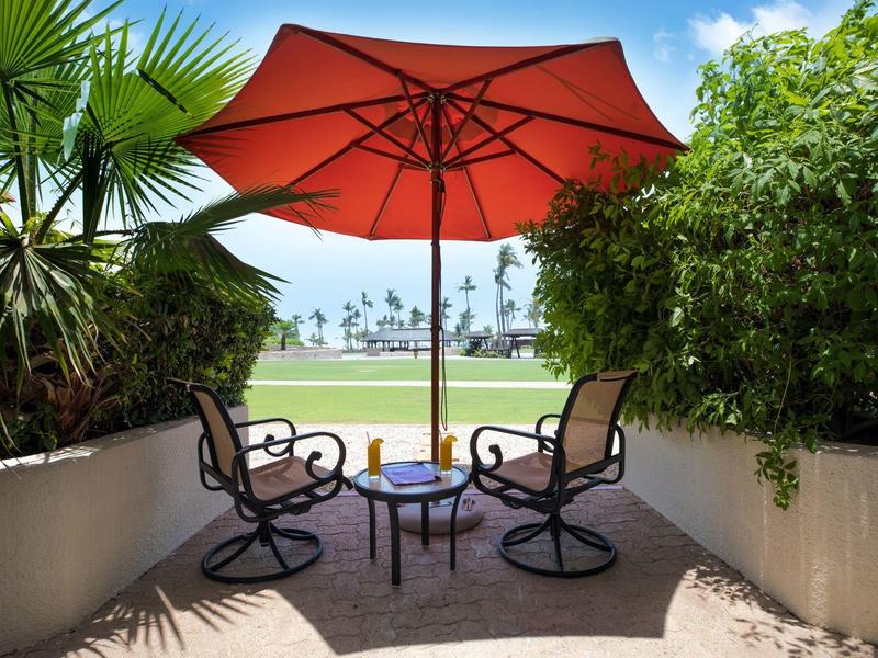 Área de descanso con sombrilla roja, dos sillas y mesa en terraza con vista al mar.