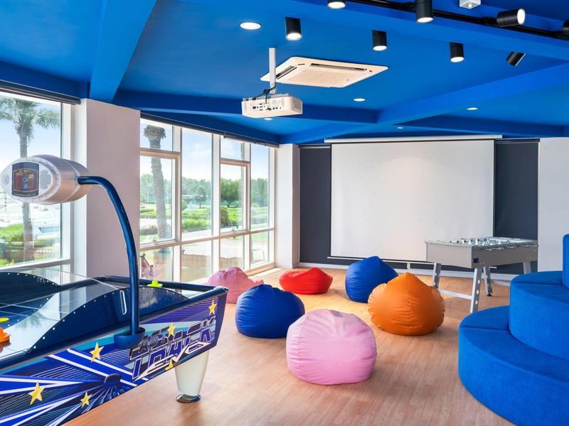 Una sala con mesa de air hockey, pufs de colores y una mesa de ping-pong frente a grandes ventanas.