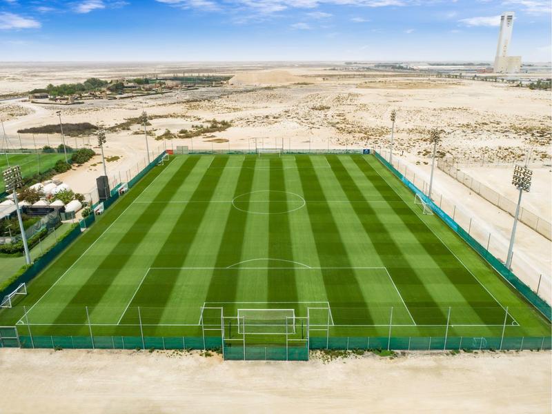 Campo de fútbol con césped bien cuidado en un área desértica con horizonte despejado.