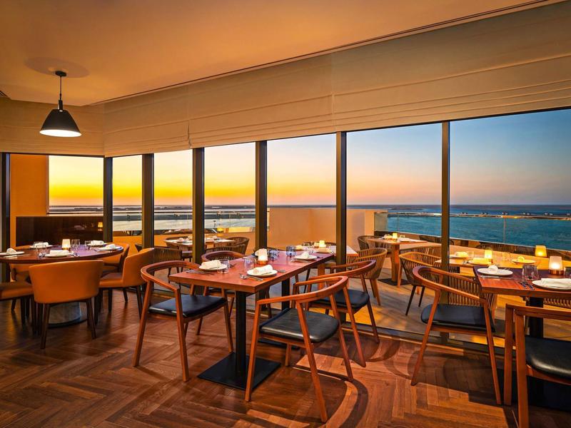 Restaurante con muebles de madera y vista al mar al atardecer a través de grandes ventanas