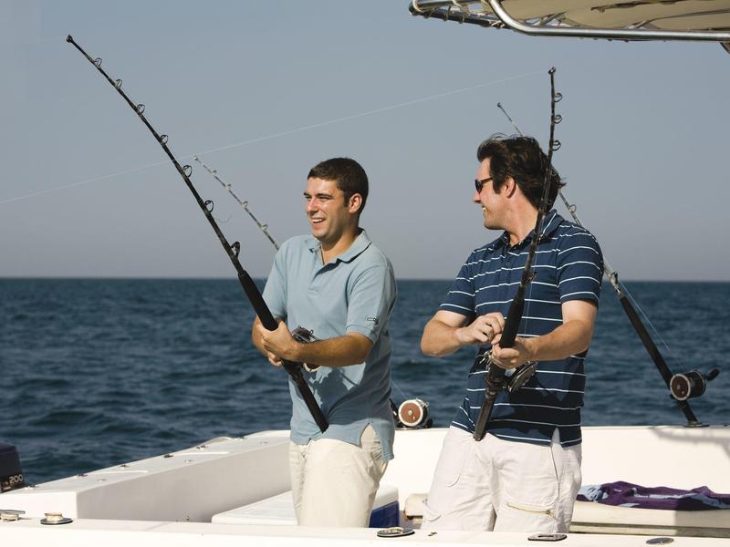 Dos hombres pescan relajados desde un barco en mar abierto bajo un cielo despejado.