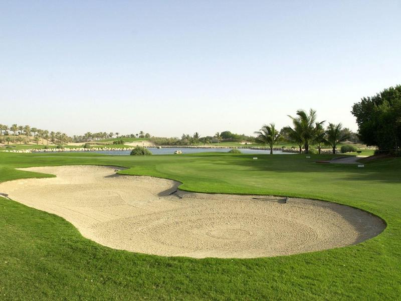 Campo de golf verde con bunker de arena y palmeras bajo un cielo despejado.