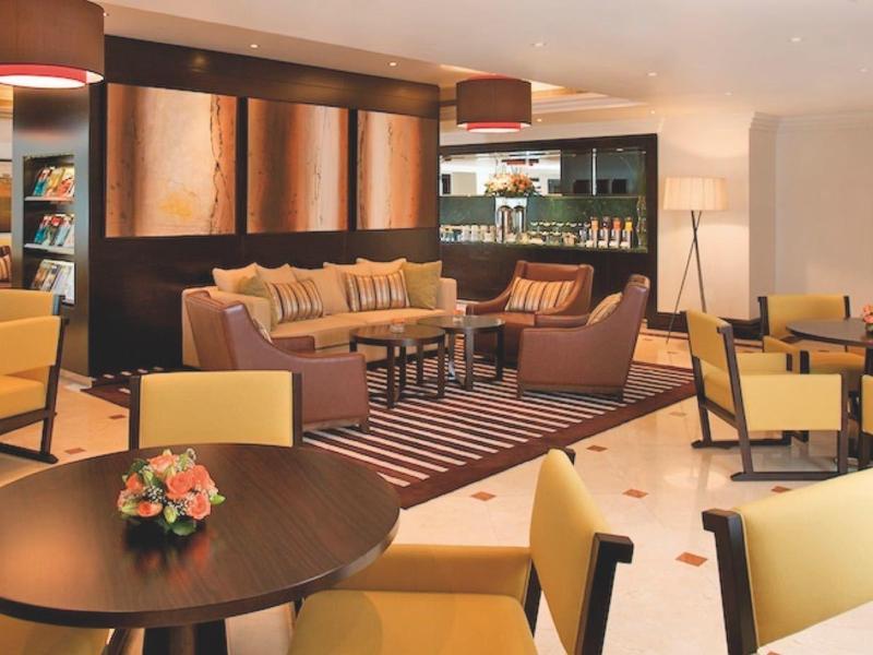 Moderner Hotel-Lounge mit gelben Sesseln, runden Tischen und warmem Licht, gemütlich und einladend.