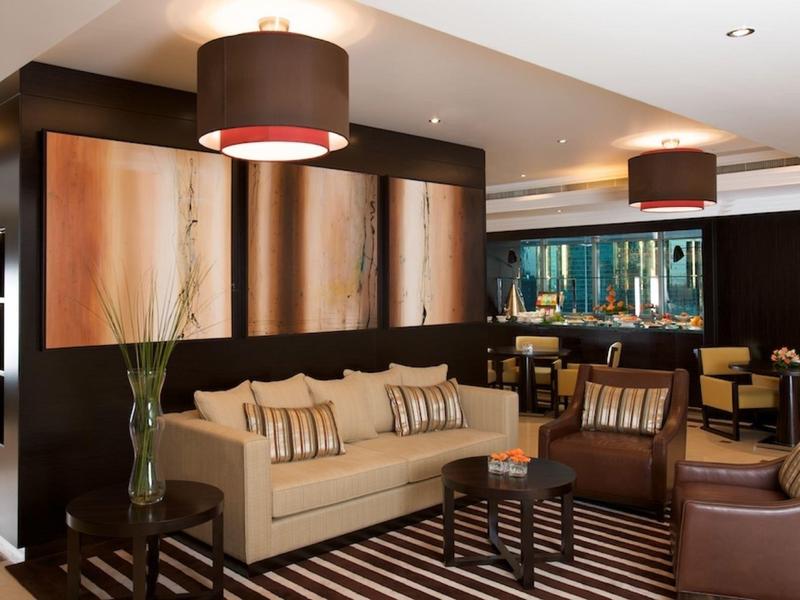 Moderner Salon mit beiger Couch, braunen Sesseln, gestreiftem Teppich und großen Deckenlampen.