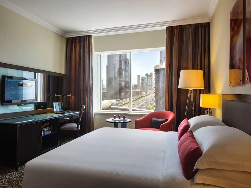 Modernes Hotelzimmer mit großem Bett, rochem Sessel, Schreibtisch und Blick auf Wolkenkratzer.