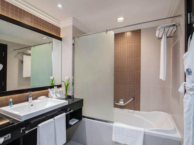 Helle, moderne Badezimmer mit weißer Badewanne, Glasduschwand, Waschbecken und großem Spiegel.