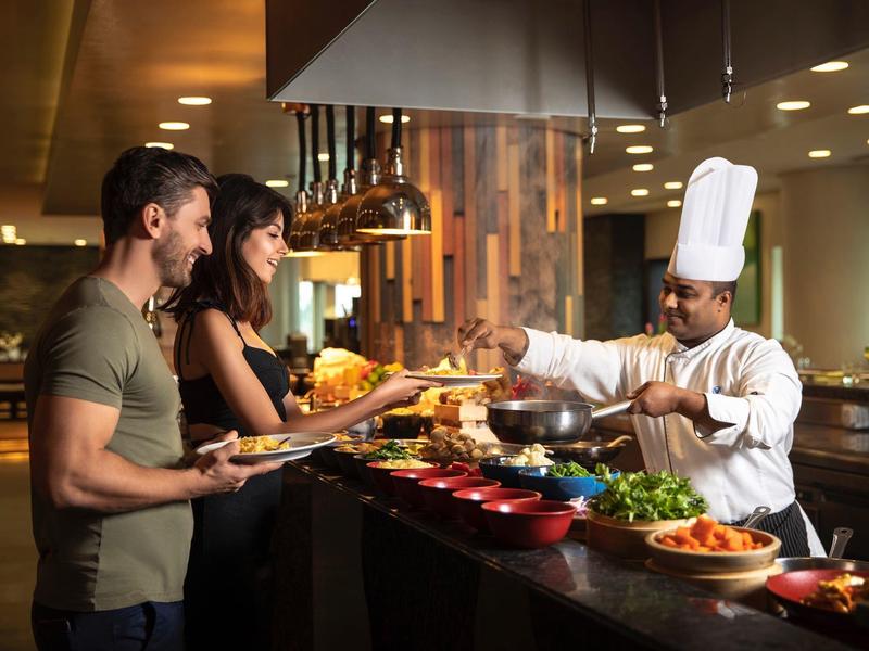 Ein Koch im weißen Hut serviert Essen einem Mann und einer Frau an einem Buffet im Restaurant.