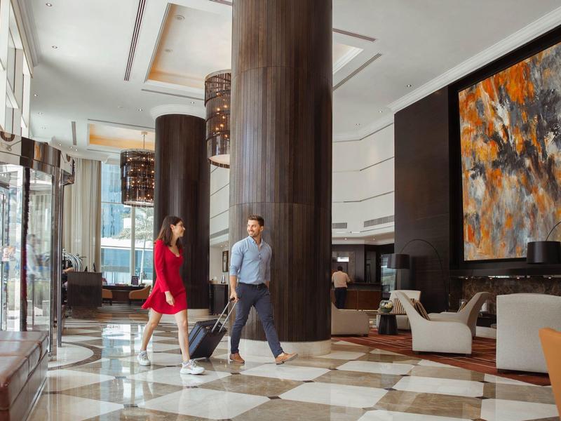 Moderne Hotellobby mit großen Säulen, großem abstraktem Gemälde und zwei reisenden Personen.