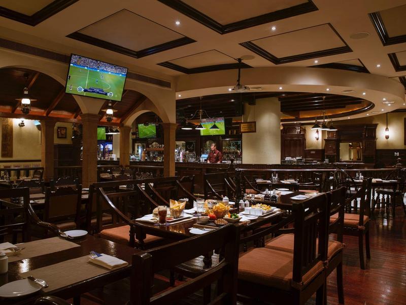 Großes, dunkles Restaurant mit Holzmöbeln, gedeckten Tischen und Bildschirmen an der Decke.