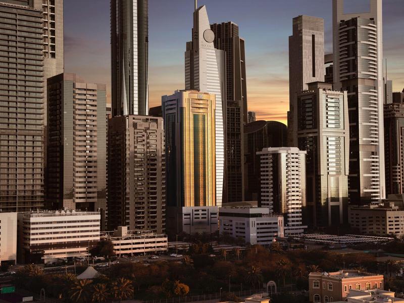 Eine Stadt mit hohen Wolkenkratzern in verschiedenen hellen und dunklen Farben bei Sonnenuntergang.