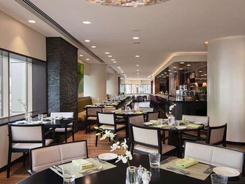 Modernes Restaurant mit hellen Wänden, dunklen Möbeln und großen Fenstern, viele gedeckte Tische.