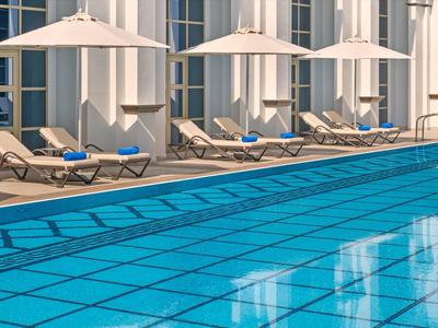 Klares Hotelpool mit Liegestühlen und weißen Sonnenschirmen am Rand.