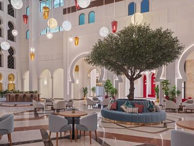 Moderna entrada de hotel con áreas de asiento, mesas redondas y un gran árbol en el centro