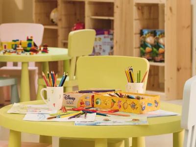 Mesa infantil colorida con material de arte y sillas en una sala de juegos.