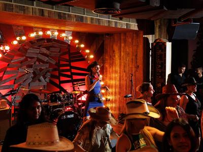 Espacio para eventos con poca luz, escenario, banda y mujer con vestido azul bailando ante el público.