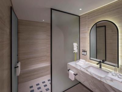 Baño moderno con paneles de madera clara, ducha grande y lavabo elegante con espejo.