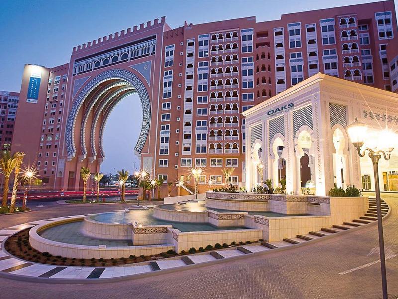 Hotel de lujo iluminado con gran entrada arqueada y fuente adyacente al anochecer.