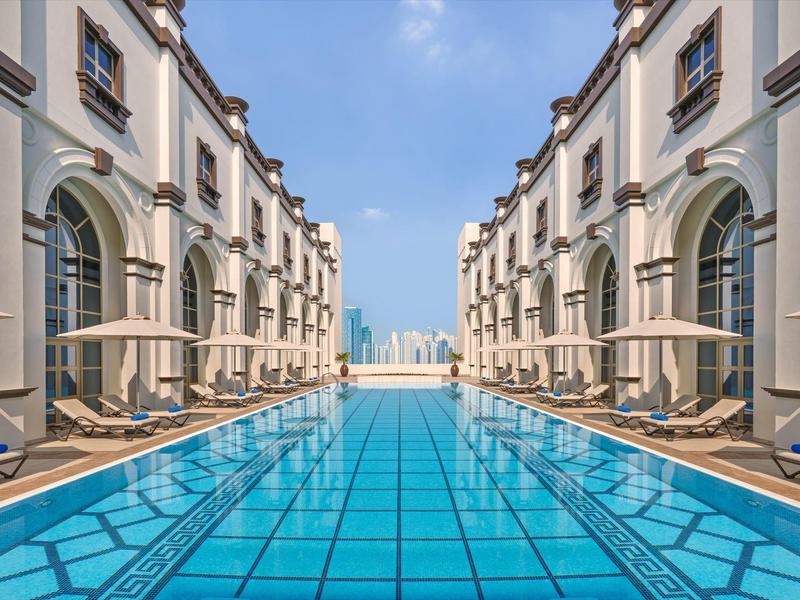 Piscina exterior moderna entre dos edificios del hotel con tumbonas y vista a la ciudad.