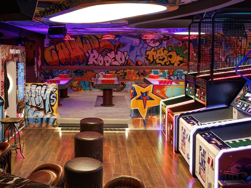 Interior de una sala de juegos con máquinas, taburetes y pared con grafitis coloridos