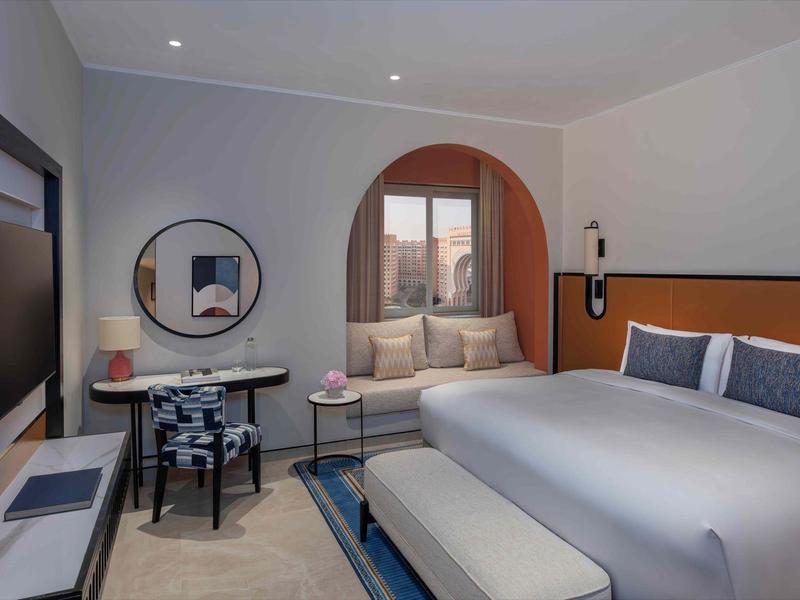 Moderna habitación de hotel con cama doble, área de estar y ventana arqueada decorativa con vista a la ciudad.