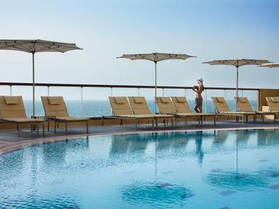 Infinity-Pool mit Sonnenschirmen und Liegen mit Meerblick an klaren Himmel.