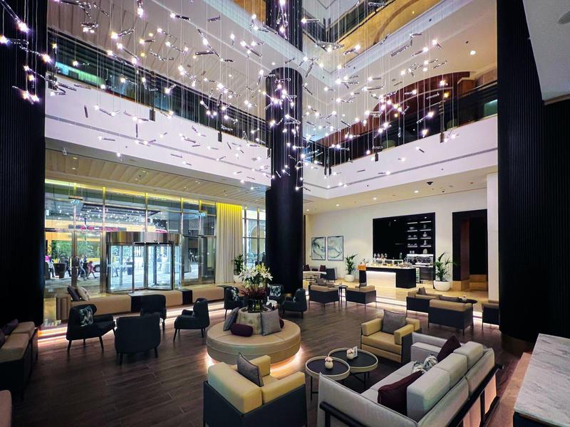 Amplia zona de lounge de hotel con muebles modernos y espacio interior de varios pisos con luces.