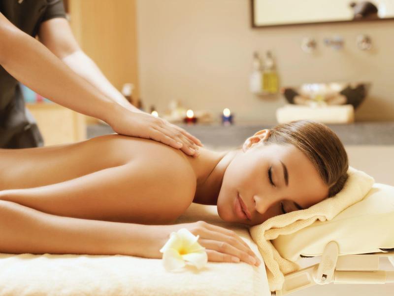 Mujer recibiendo masaje relajante en la espalda en una sala de spa luminosa con velas y toallas.