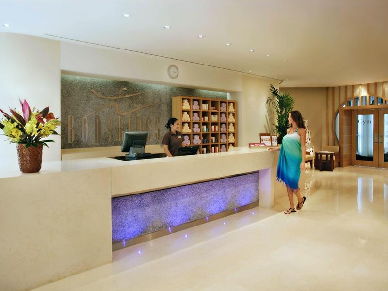 Recepción de hotel con mostrador moderno, planta decorativa y persona atendiendo a huésped.