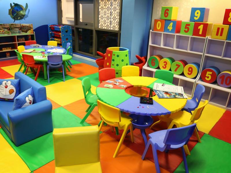 Sala de juegos infantil colorida con sillas pequeñas, mesas y estantes llenos de juguetes en un hotel.