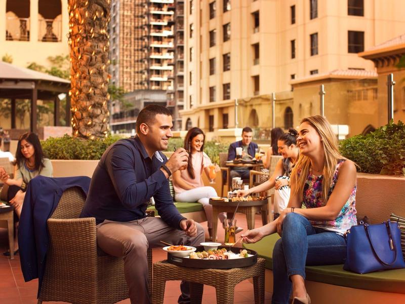 Un grupo de personas sentadas relajadas en la terraza de un hotel con aperitivos en la mesa.