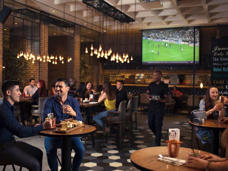 Restaurante elegante con luces colgantes, clientes cenando y un partido de fútbol en televisión