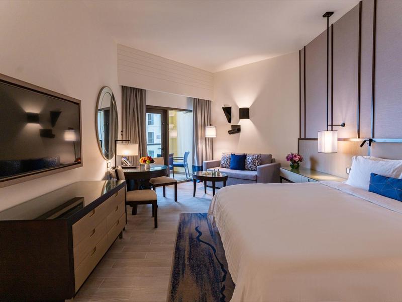 Habitación de hotel moderna con cama grande, televisión y zona de estar junto a la ventana.