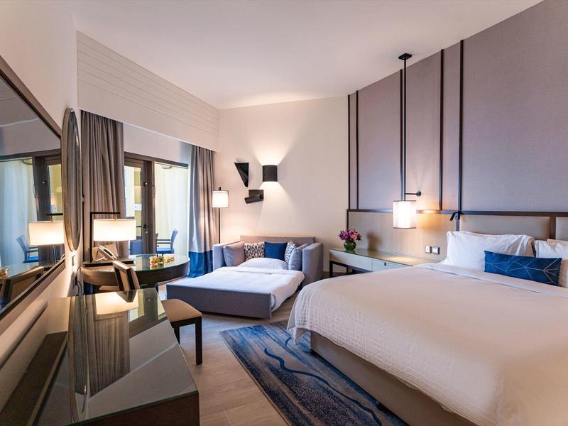 Habitación de hotel moderna con dos camas, área de estar y luz cálida.