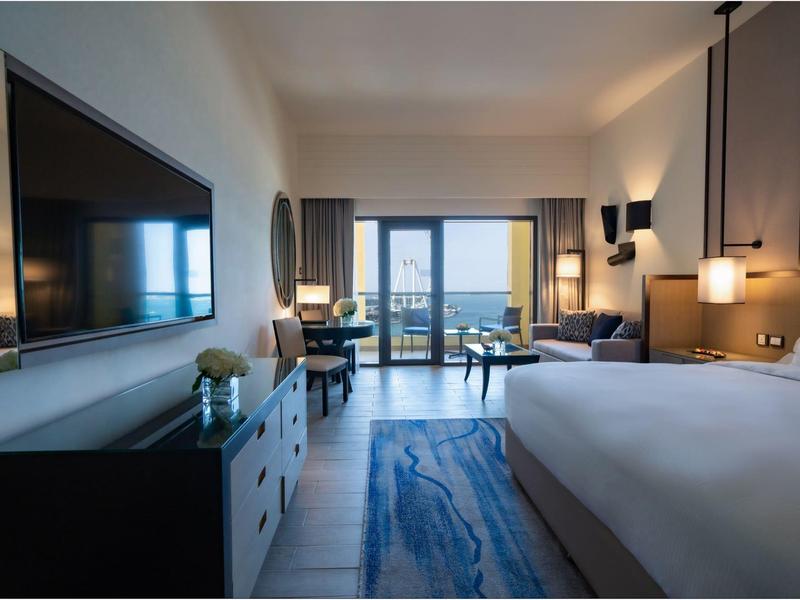 Habitación de hotel moderna con cama grande, TV, escritorio y balcón con vista al mar.