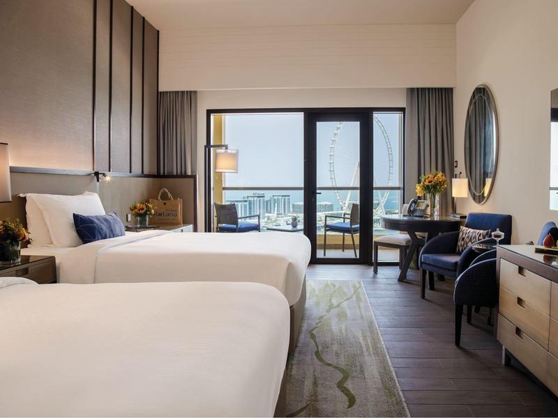 Habitación de hotel luminosa con dos camas, balcón y vista al mar durante el día.