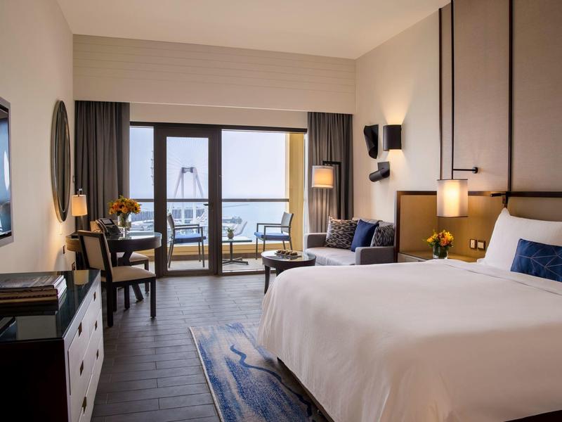 Habitación de hotel luminosa con cama grande, escritorio y balcón con vista al mar.