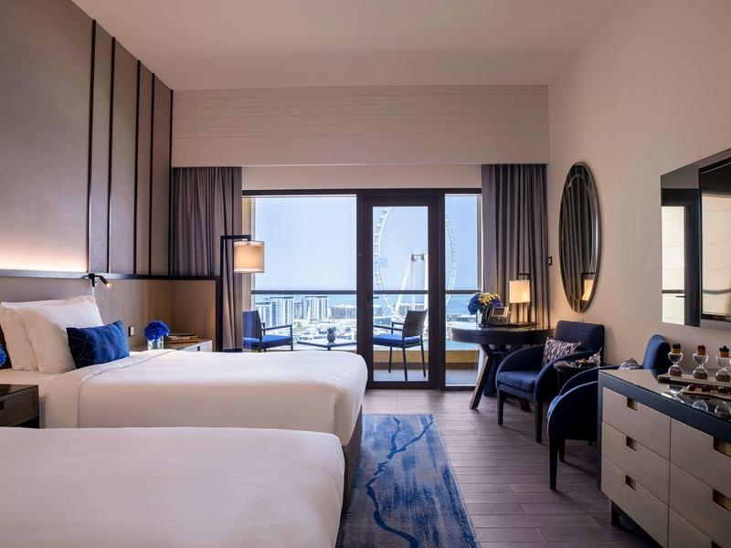 Habitación de hotel moderna con dos camas, decoración azul y balcón con vistas.