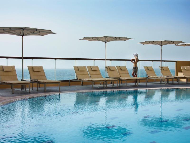 Área de piscina con tumbonas y sombrillas junto al mar bajo un cielo despejado.
