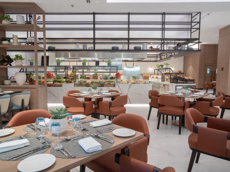 Restaurante moderno con detalles de madera y metal, mesas puestas y sillas acolchonadas en tono marrón.