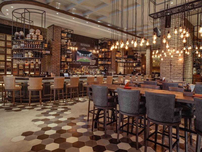 Bar elegante de hotel con taburetes modernos, estantes de madera y iluminación ambiental.