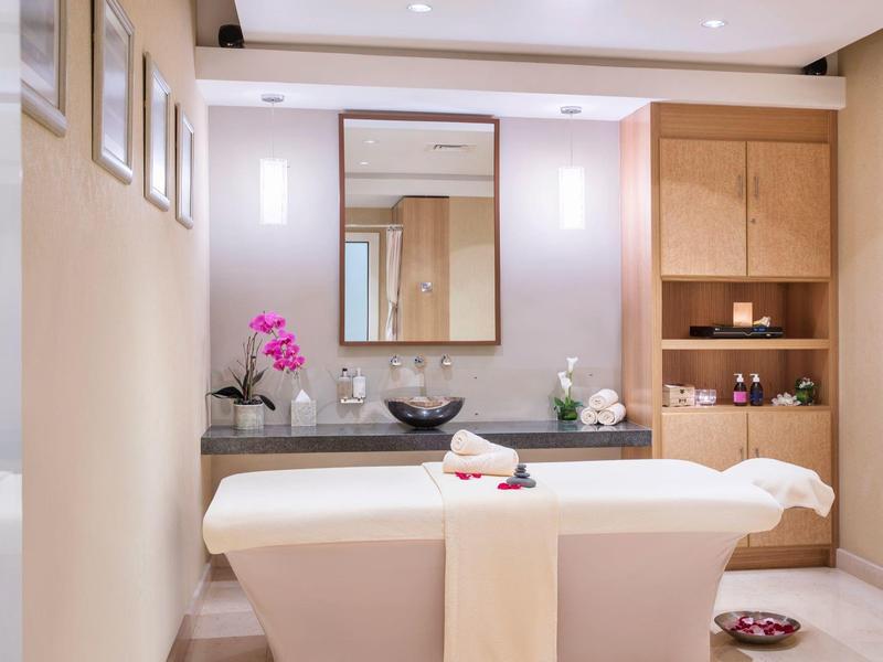 Sala de masajes luminosa con camilla, espejo y orquídea en ambiente suave.