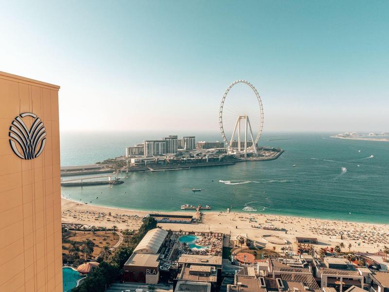 Vista de una ciudad costera con grandes edificios, playa y una noria en el mar.