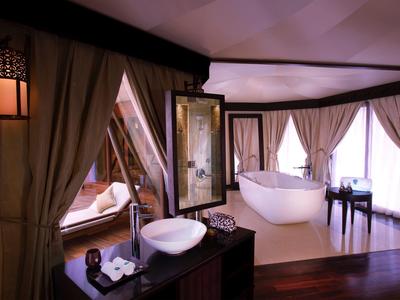 Luxuriöses Zimmer mit freistehender Badewanne, Waschbecken und Holzboden in warmen Farben.