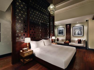 Elegantes Schlafzimmer mit großem Bett, dunklem Holz, orientalischem Wandmuster und warmem Licht.