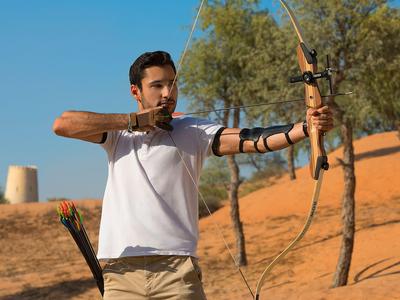 Mann schießt mit einem Bogen in einer Wüstenlandschaft unter klarem Himmel.