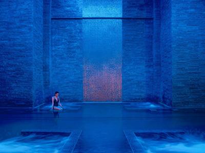 Person entspannt sich in einem gedämpft beleuchteten blauen Pool im Innenbereich.