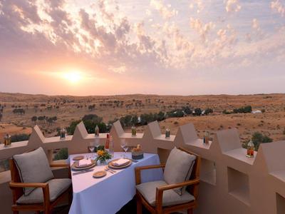 Terrasse mit gedeckten Tischen bietet Blick auf eine Wüstenlandschaft bei Sonnenuntergang.